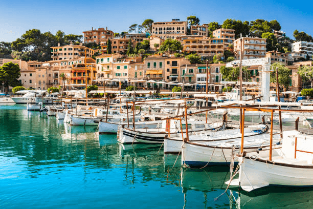 Exklusiver Yachthafen auf den Balearen mit zahlreichen Segelyachten und traditionellen Booten vor mediterraner Architektur. Beliebtes Revier für Yachtcharter, Segelurlaub auf Mallorca und luxuriöse Törns entlang der Küsten des Mittelmeers.