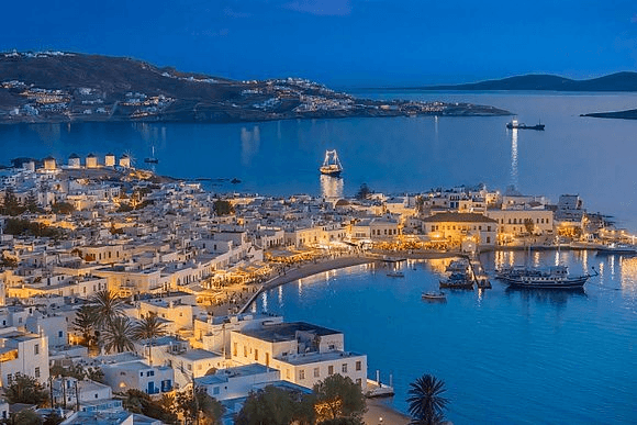 Beleuchteter Hafen von Mykonos bei Nacht mit Segelbooten und typisch weißen Häusern am Wasser