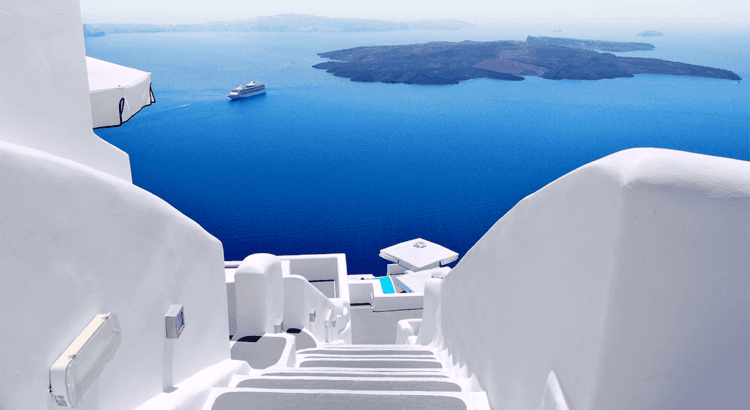 Weiße Treppen und traditionelle Kykladen-Architektur mit Blick auf das tiefblaue Meer und eine Luxusyacht vor Santorini in Griechenland – exklusiver Yacht Charter und Segelurlaub in der Ägäis.