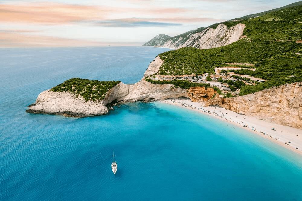 Türkisfarbene Bucht in Lefkada mit weißem Sandstrand, steilen Klippen und Segelyacht vor der Küste von Griechenland – traumhafter Yacht Charter und Segelurlaub im Ionischen Meer.