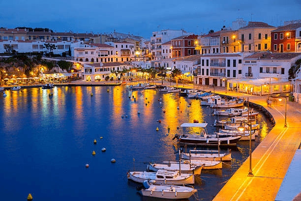 Der Naturhafen von Mahón auf Menorca mit Segelyachten entlang der Uferpromenade und mediterraner Architektur. Idealer Startpunkt für einen Segelurlaub und Yachtcharter auf den Balearen.